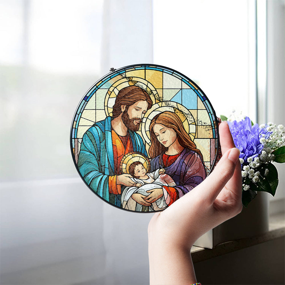 A hand holds a circular stained-glass-style window ornament depicting Jesus, Mary, and baby Jesus. Christian Christmas Holy Family glass suncatcher for window decor