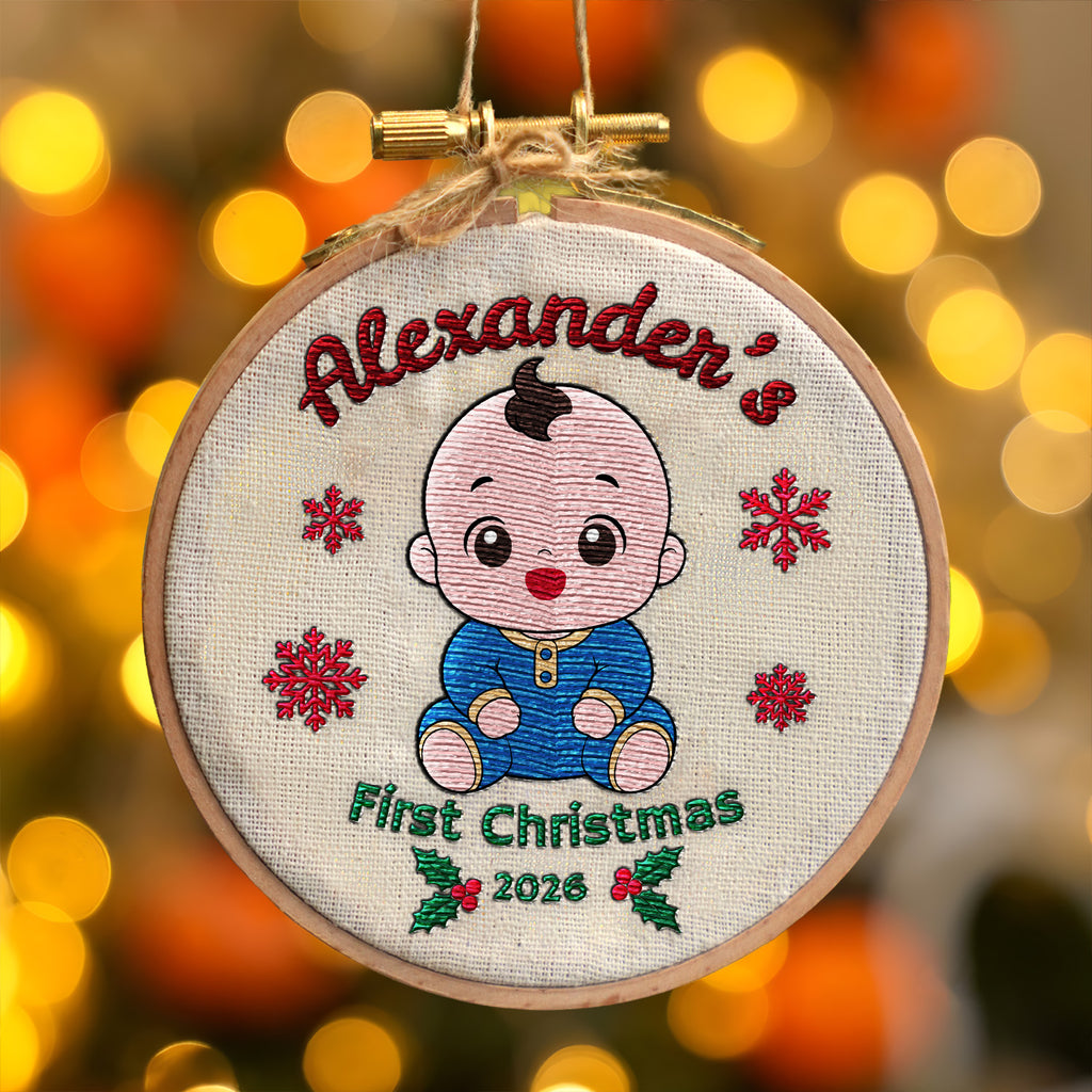 Personalized baby first Christmas embroidered hoop ornament showing smiling baby, red snowflakes and holly displayed with gold hanger and Christmas lights