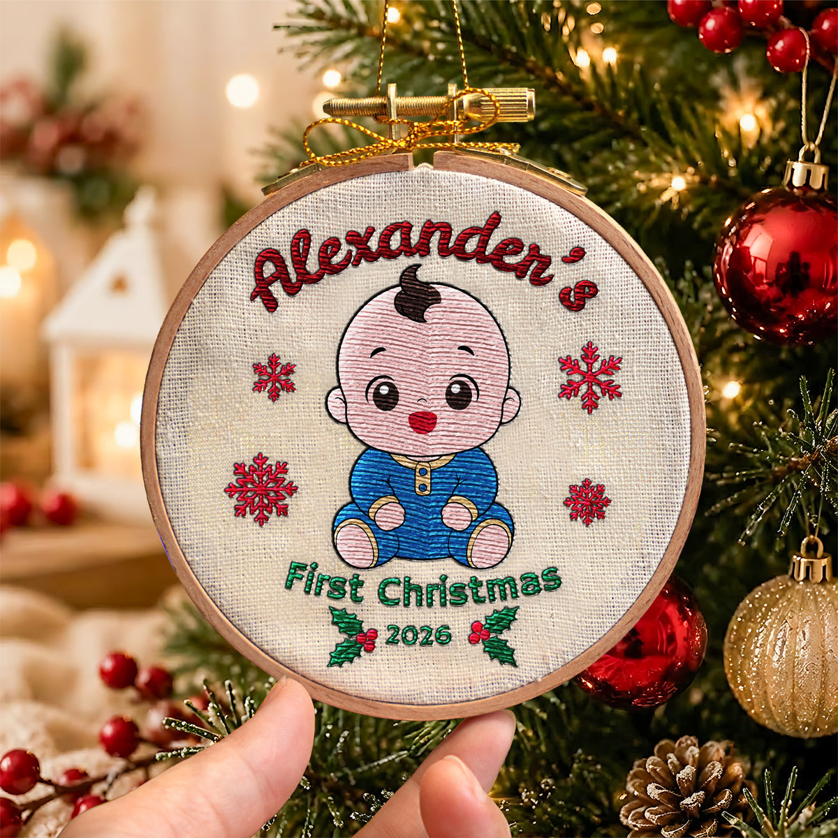 Personalized baby first Christmas embroidered hoop ornament showing smiling baby, red snowflakes and holly hanging on Christmas tree with gold hanger